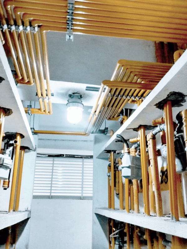 Nova tubulação de gás instalada em área técnica de edificação, com rede de tubos amarelos e medidores.